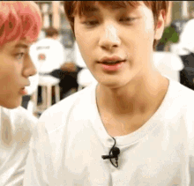 a man with pink hair is talking to another man while wearing a white t-shirt and a microphone .