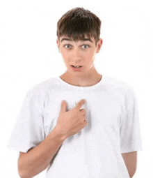a young man in a white t-shirt is pointing at his chest with his hand .