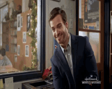 a man in a suit is smiling in front of a hallmark movie and a christmas tree