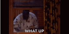 a man in pajamas is looking out of a window and the words what up are on the screen