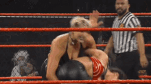 two women are wrestling in a ring while a referee watches .
