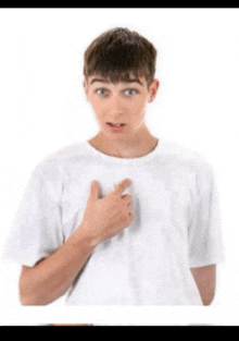 a young boy in a white t-shirt is pointing at his chest