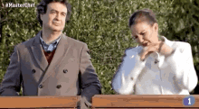 a man and a woman are standing next to each other on a bench with the number 1 on it .