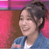 a woman wearing a denim jacket is smiling in front of a pink background ..