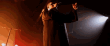 a man in a black coat is singing into a microphone