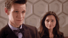 a man in a suit and bow tie looks at a woman