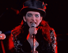 a woman is singing into a microphone while wearing a top hat .