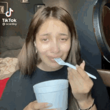 a woman is crying while eating from a styrofoam cup with a fork in her mouth .