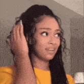 a woman in a yellow shirt is wearing headphones and making a funny face .