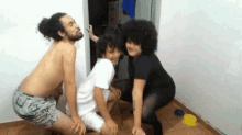 a group of people are squatting on the floor including a shirtless man and two women