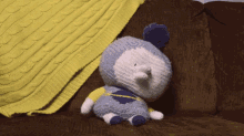 a stuffed animal is sitting on a couch with a yellow blanket behind it