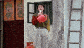 a man is holding a red watering can in his hand while standing in front of a building .