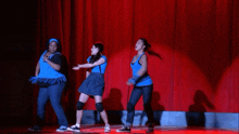 three women in blue shirts are dancing on a stage