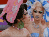 a drag queen is kissing another drag queen while wearing a pink hat
