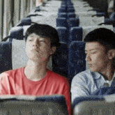 two young men are sitting next to each other on a bus and one of them is sleeping .