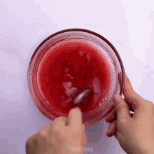 a person is mixing a red liquid in a bowl with a spoon