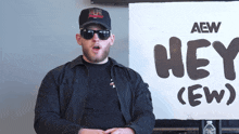 a man wearing sunglasses stands in front of a sign that says hey