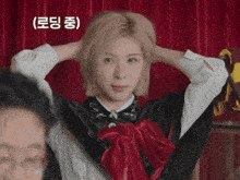 a woman in a black cape with a red bow holds her hands to her head