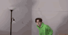 a man in a green hoodie and brown pants is jumping in a room .