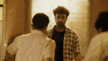 a man in a plaid shirt is talking to another man in a black shirt .
