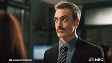a man in a suit and tie with a nbc logo on his chest