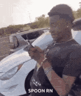 a man is standing in front of a white car while looking at his phone .