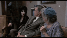 a woman in a black dress is sitting next to a man and woman