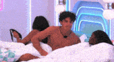 a man without a shirt is laying on a bed next to two women .