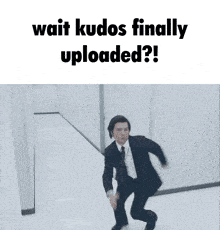 a man in a suit and tie is running down a hallway with the words wait kudos finally uploaded below him