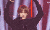 a man in a black jacket stands on a stage with his arms in the air and a sbs logo behind him