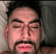 a man with a beard is laying in bed with his eyes closed .