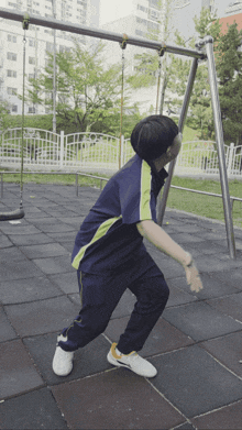 a boy in a blue and yellow shirt is standing on a tiled floor in front of a swing set