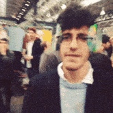 a man wearing glasses and a jacket stands in a crowd