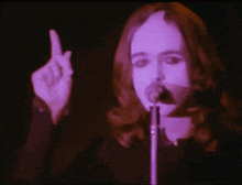 a woman with long hair singing into a microphone with purple lights behind her