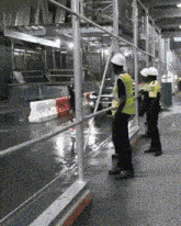 two men wearing hard hats and safety vests are standing in a wet area