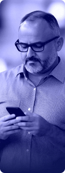 a man with glasses and a beard is looking at his cell phone in a blue background .