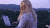 a woman with long blonde hair is using a laptop computer outdoors