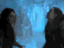 two women standing next to each other in a dark room with a blue light behind them