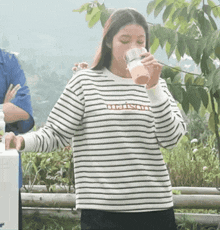 a woman wearing a striped shirt drinking from a cup with the word mission written on it
