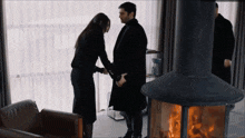 a man and woman are shaking hands in front of a fireplace
