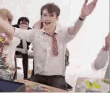 a man in a school uniform and tie is sitting at a table with his arms outstretched .