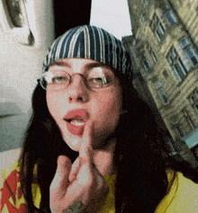 a woman wearing glasses and a striped hat is making a middle finger gesture
