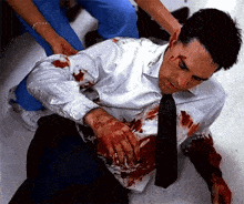 a man in a white shirt and tie is laying on the floor covered in blood