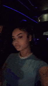 a woman wearing a blue shirt and a gold necklace is making a funny face while sitting in a car .