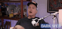 a man wearing a hat is talking into a microphone in front of a dark web sign .