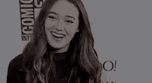 a woman with long brown hair is smiling in front of a comic con logo .