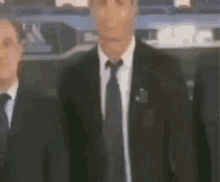 a man in a suit and tie is standing next to two other men in suits and ties .
