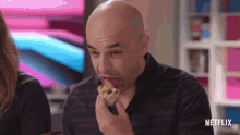 a bald man is eating a donut with a netflix logo on the bottom