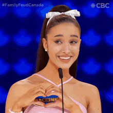 a woman making a heart shape with her hands in front of a microphone with the hashtag familyfeudcanada