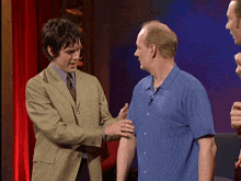 a man in a blue shirt is talking to another man in a green suit